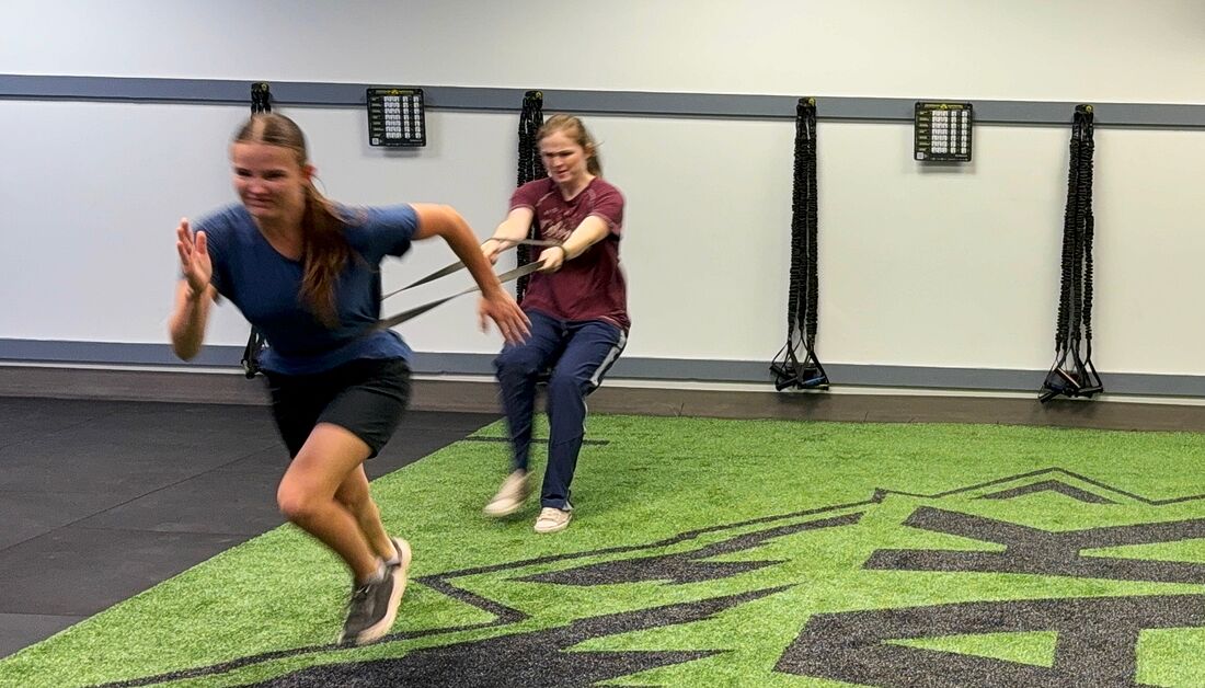 Athlete driving out of a band-resisted sprint while her partner holds the band